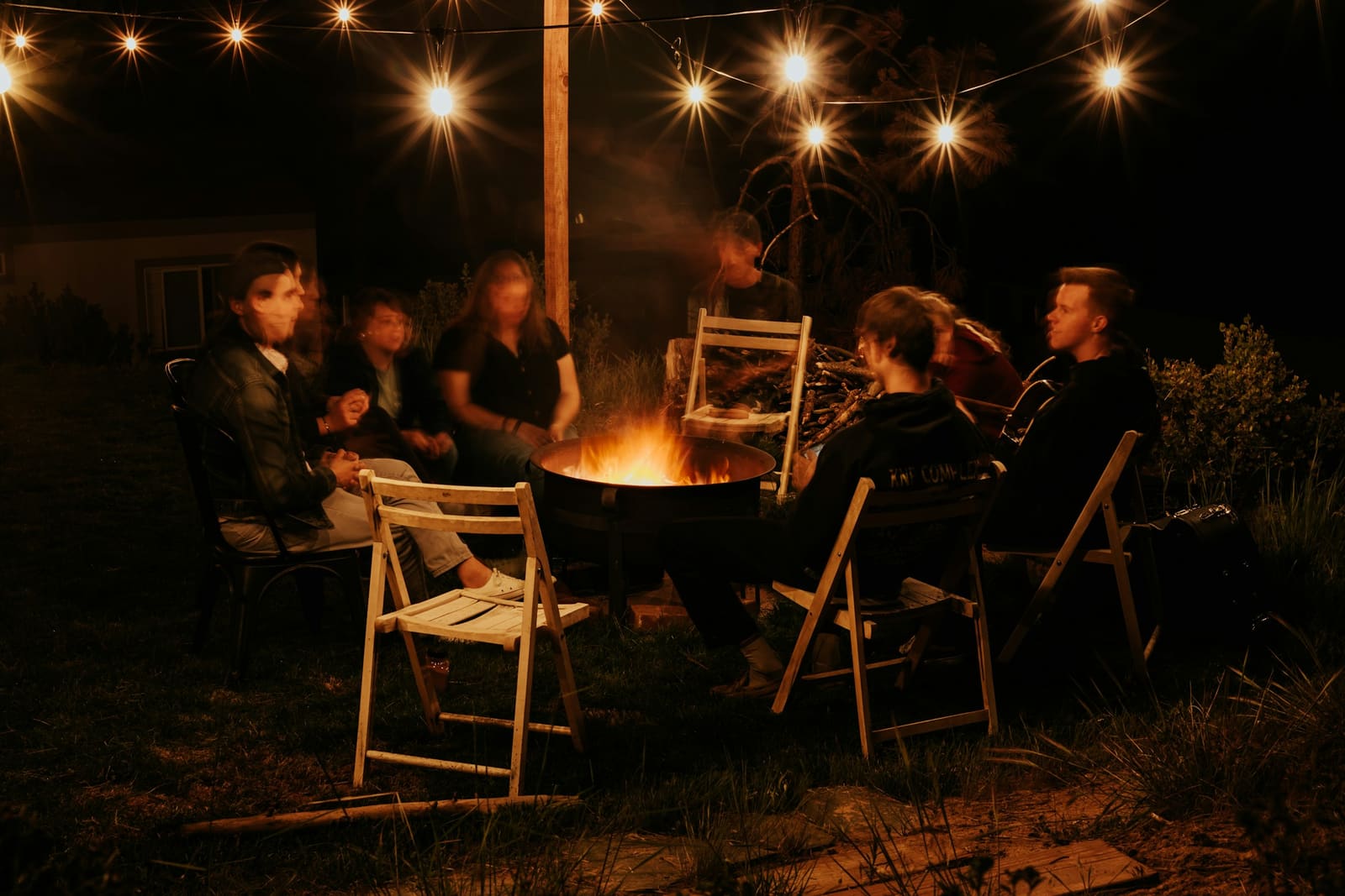 Family of all ages gathered around a fire pit under string lights at night